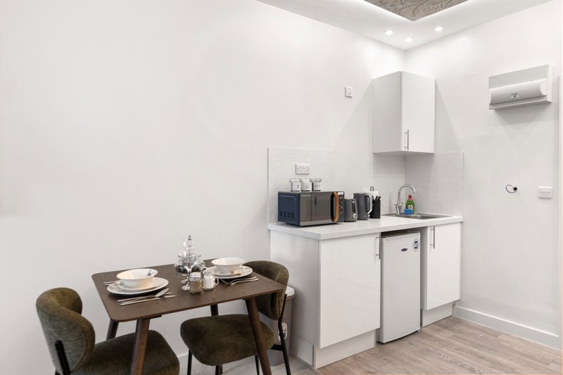 Modern kitchenette with dining table, two chairs, white cabinetry and appliances
