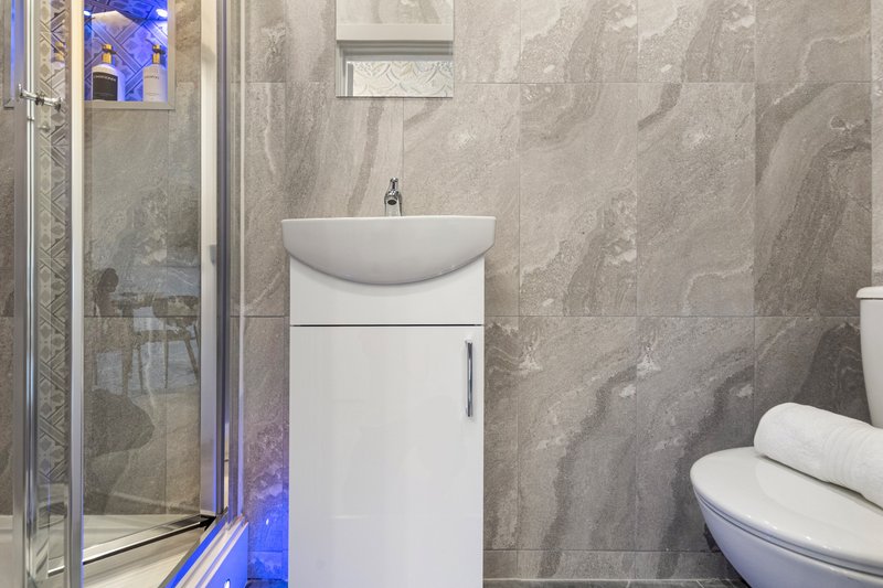 Modern bathroom with white vanity sink, gray tile walls, shower enclosure and toilet