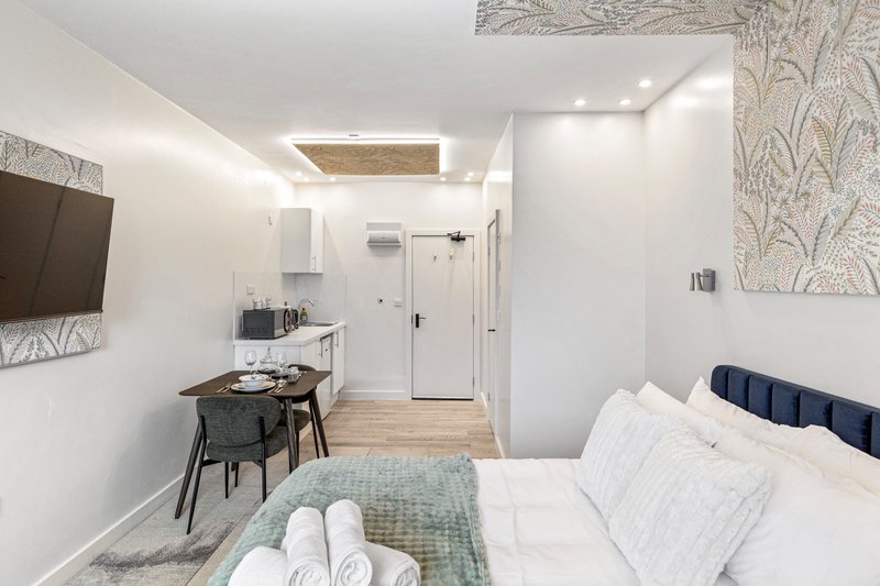 Modern studio bedroom with double bed, desk area, kitchenette and wall-mounted TV