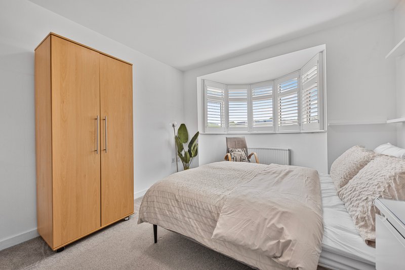 Bright bedroom with double bed, wooden wardrobe, and shuttered bay window