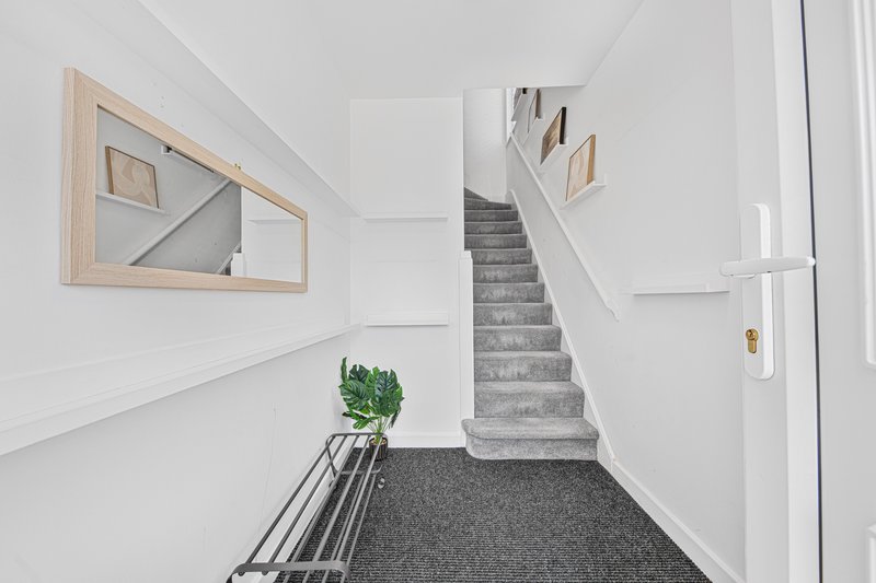 Bright hallway with staircase, wooden mirror, potted plant and cozy carpet