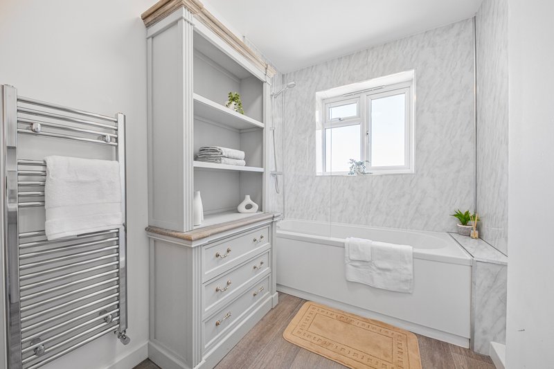 Modern bathroom with marble walls, white storage cabinet, heated towel rail and wooden floor
