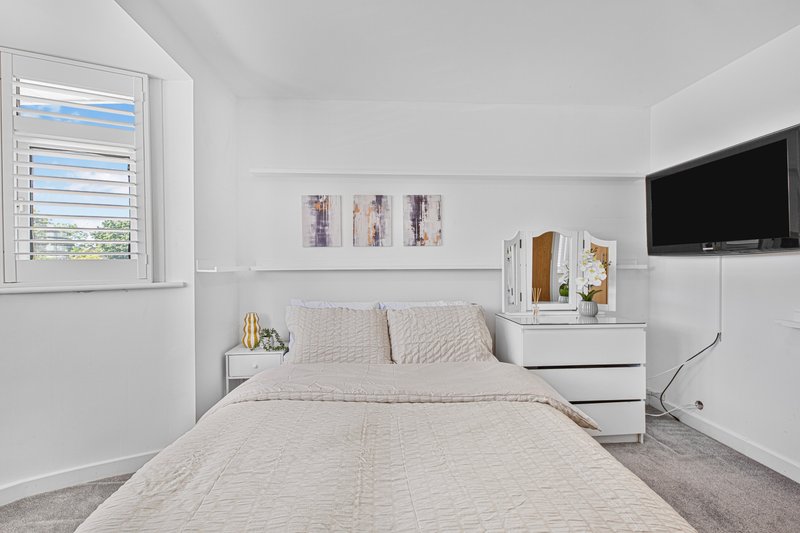 Bright modern bedroom with double bed, white furniture, wall-mounted TV and window with shutters