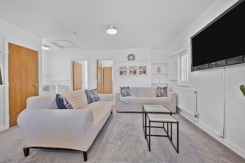 Bright living room with cream sofas, armchair, coffee table, wall-mounted TV and wooden doors