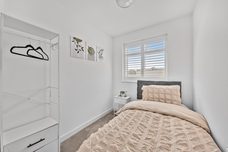 Modern bedroom with single bed, bedside table, ensuite shower, and shuttered window