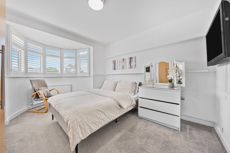 Bright modern bedroom with double bed, white dresser, shuttered window seat and wall-mounted TV
