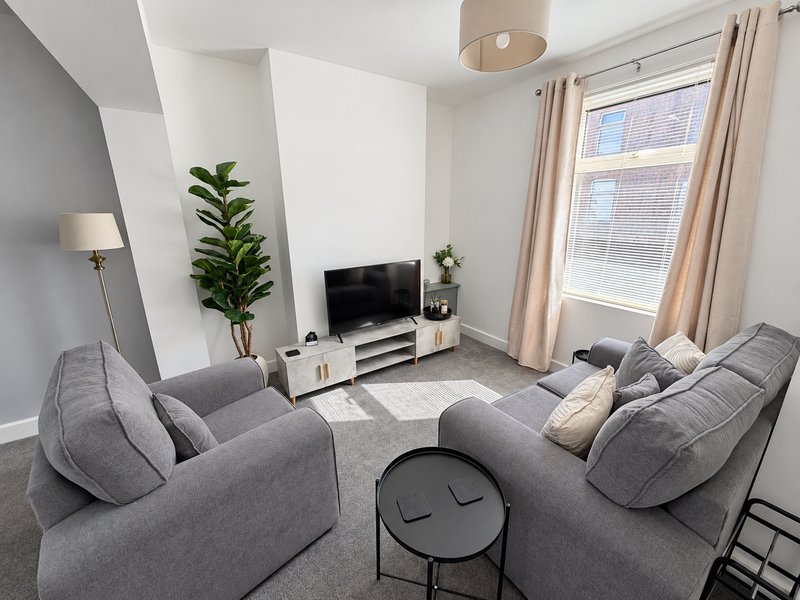 Modern living room with gray sofas, TV stand, potted plant, and large window with curtains