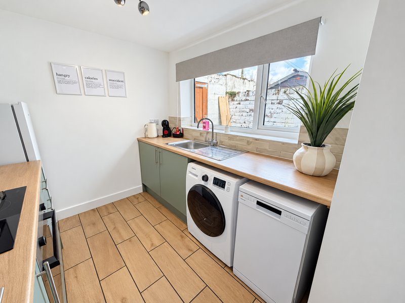 Modern kitchen with washer, dishwasher, wooden countertop and window overlooking garden