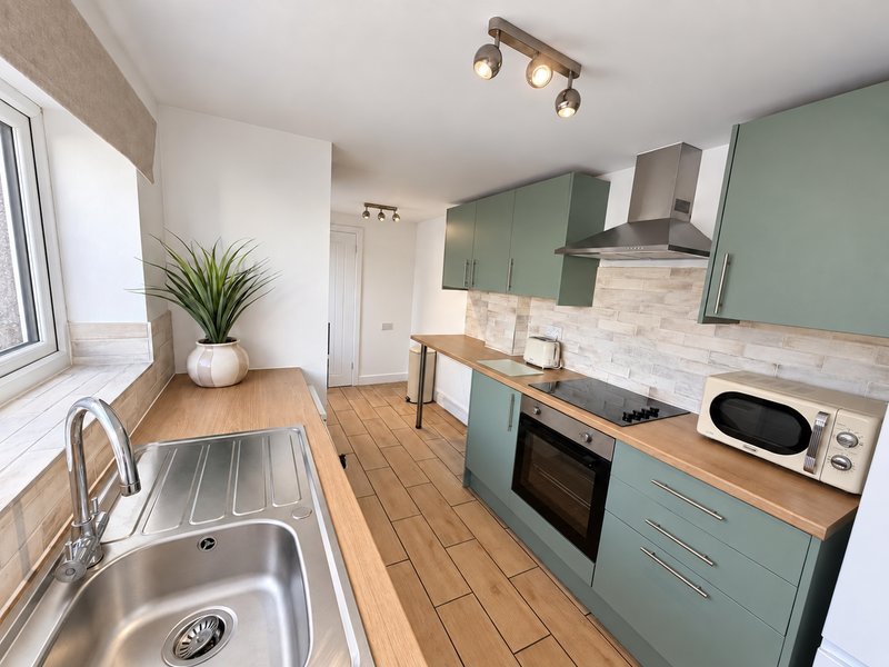 Modern kitchen with green cabinetry, wooden countertops, stainless steel sink and appliances