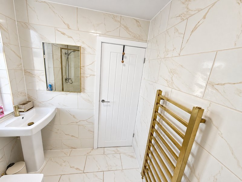 Modern bathroom with cream marble tiles, pedestal sink, mirror, shower enclosure and gold towel rail