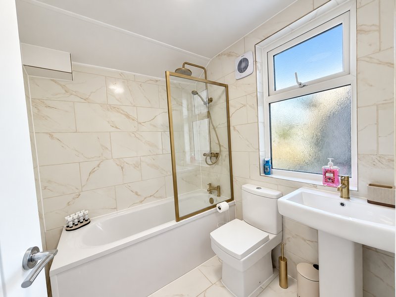 Modern bathroom with marble-effect tiling, bathtub with glass shower enclosure, pedestal sink and window
