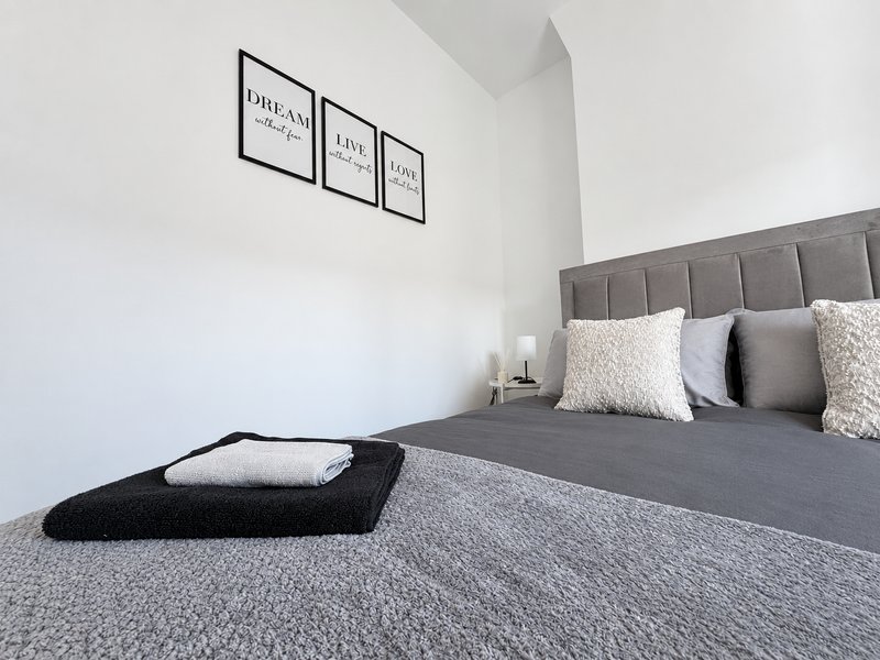 Modern bedroom with gray upholstered headboard, white pillows, dark bedding, and wall art