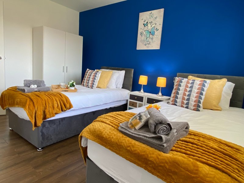 Modern bedroom with two beds, blue accent wall, yellow bedding and decorative pillows