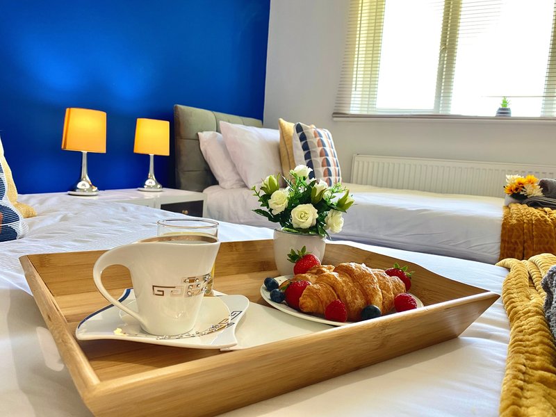 Bright bedroom with blue accent wall, bed with pillows, wooden tray with coffee cup and fresh fruit