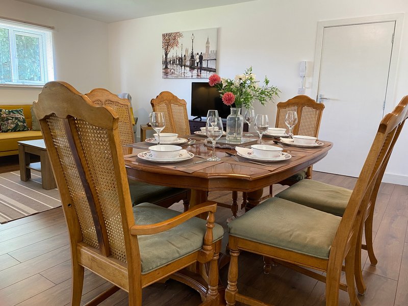 Dining room with wooden table, upholstered chairs, place settings, and floral centerpiece