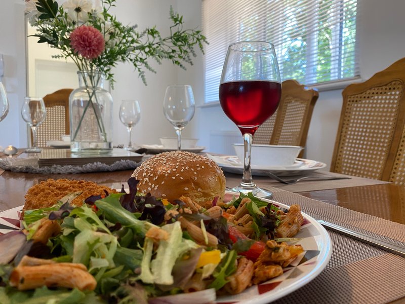 Dining table set with burger, salad, wine glass and flower arrangement