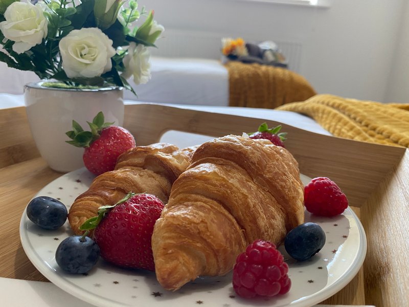 Kitchen counter with croissants, fresh berries, white flowers in vase and yellow cushioned chair