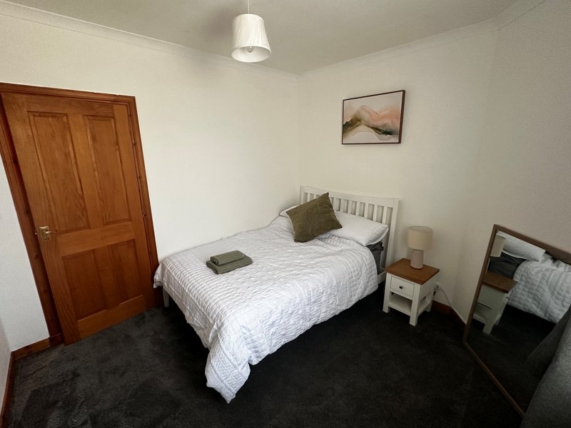 Bedroom with double bed, bedside table, chest of drawers and rear facing window.