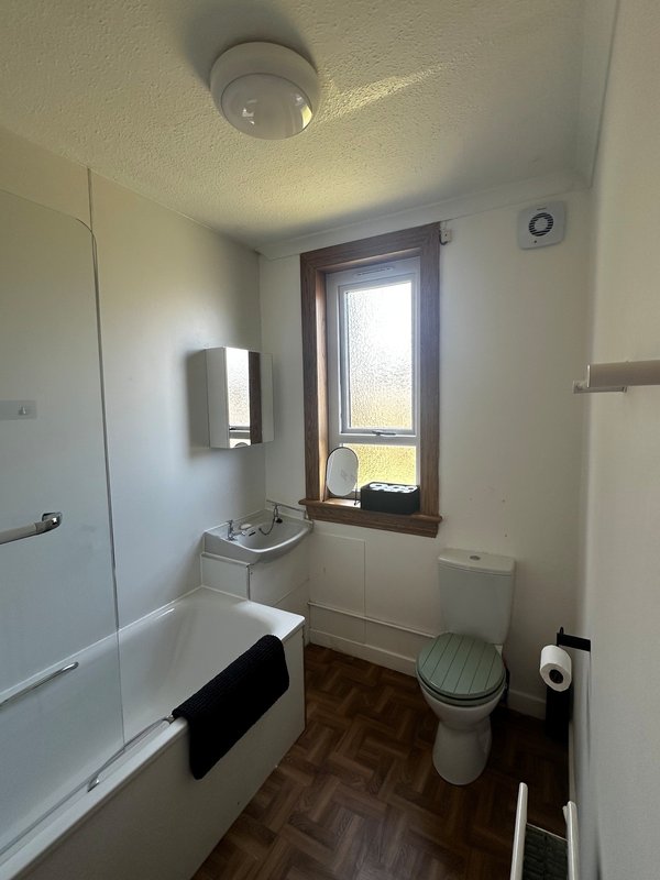 Bathroom with toilet, sink, over-bath shower and rear facing window.