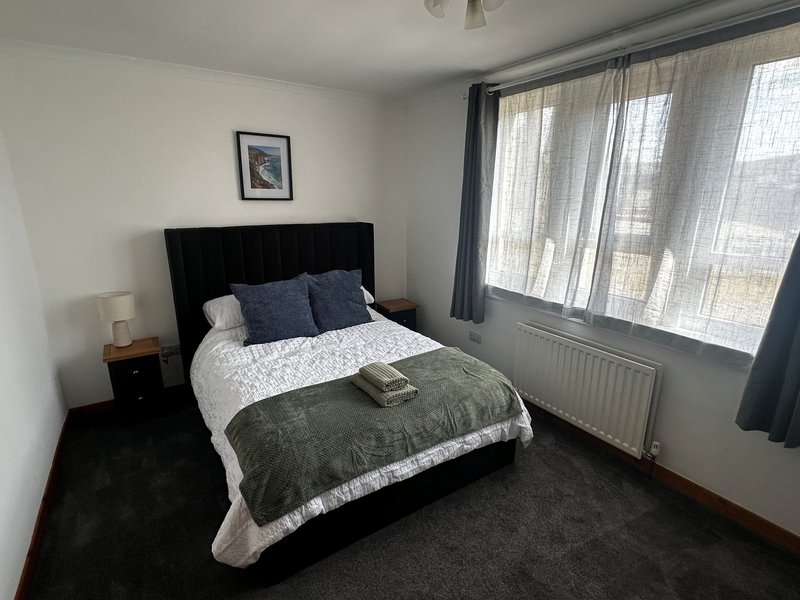 Bedroom with king size bed, bedside tables, chest of drawers, hanging space and large front facing windows.