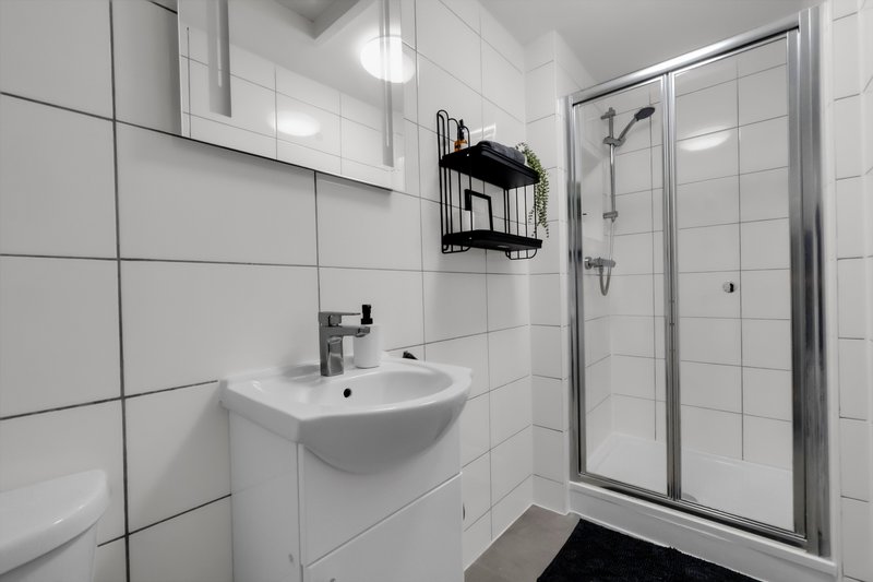 Modern bathroom with white tiles, wall-mounted sink, shower enclosure and black storage caddy