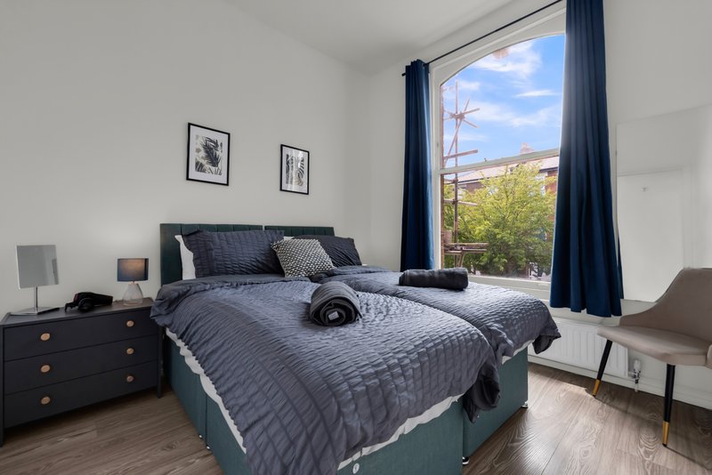Modern bedroom with double bed, dark bedding, wooden nightstands, and large window with countryside view