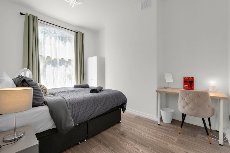 Bright bedroom with double bed, wooden floor, desk chair and window with curtains