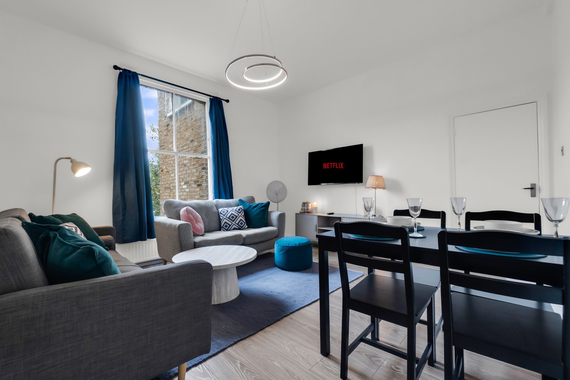 Open-plan living and dining room with grey sofa, blue armchair, black dining table and wall-mounted TV