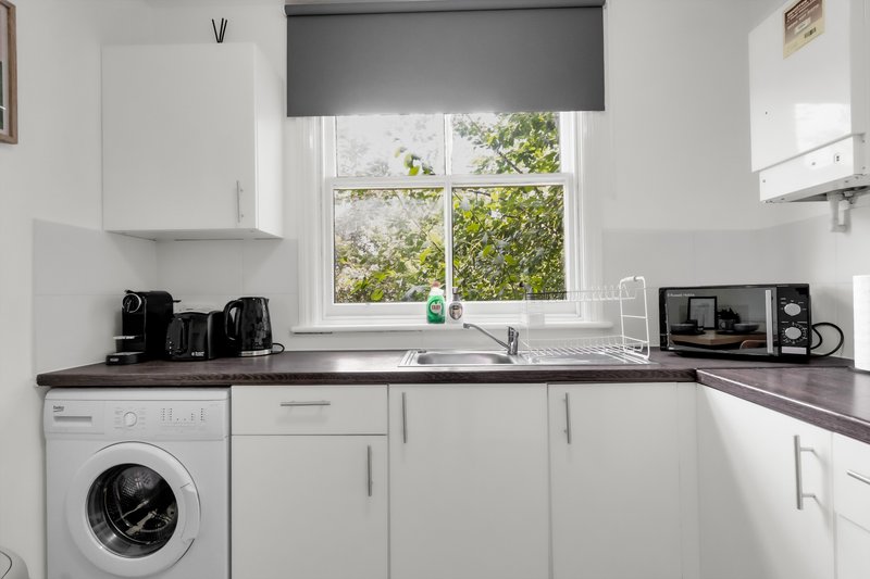Modern kitchen with white cabinetry, dark countertop, washing machine, window with garden view
