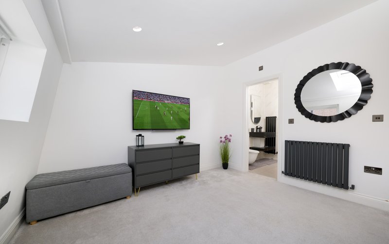 Modern living room with gray sofa, wall-mounted TV, dark dresser and decorative mirror