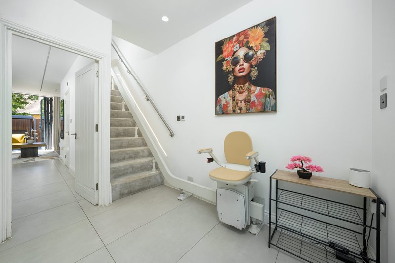 Modern hallway with stairs, white walls, framed artwork, and furnished seating area