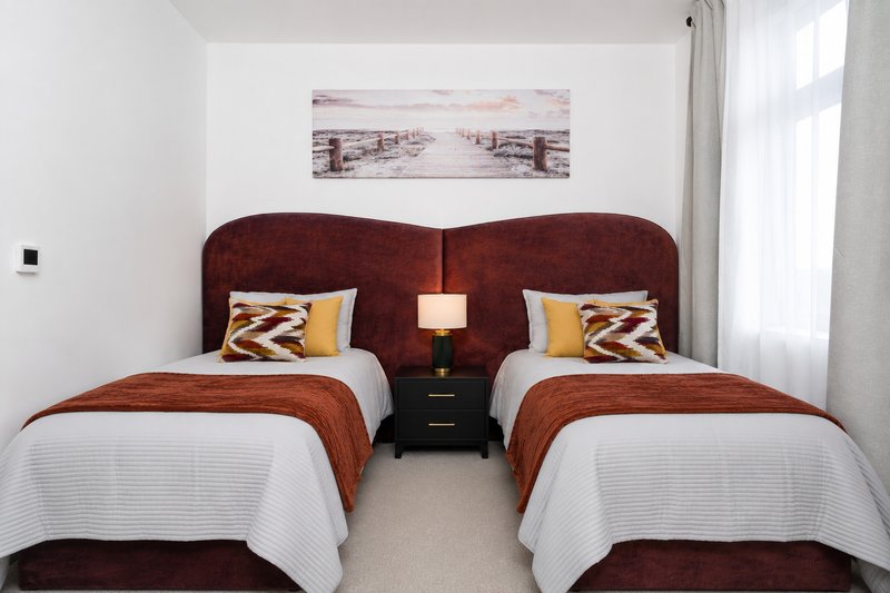 Twin bedroom with burgundy headboards, white bedding, patterned cushions and shared bedside table