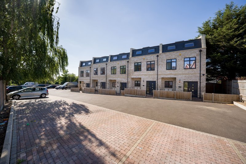 Modern brick residential building with multiple units, paved courtyard and parked cars