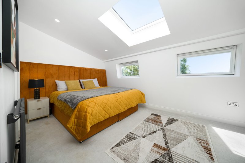Modern bedroom with yellow bed, wooden headboard, skylight, and geometric patterned rug