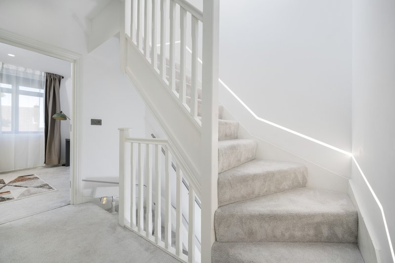 Bright staircase with white railings, grey carpet, and natural light from window