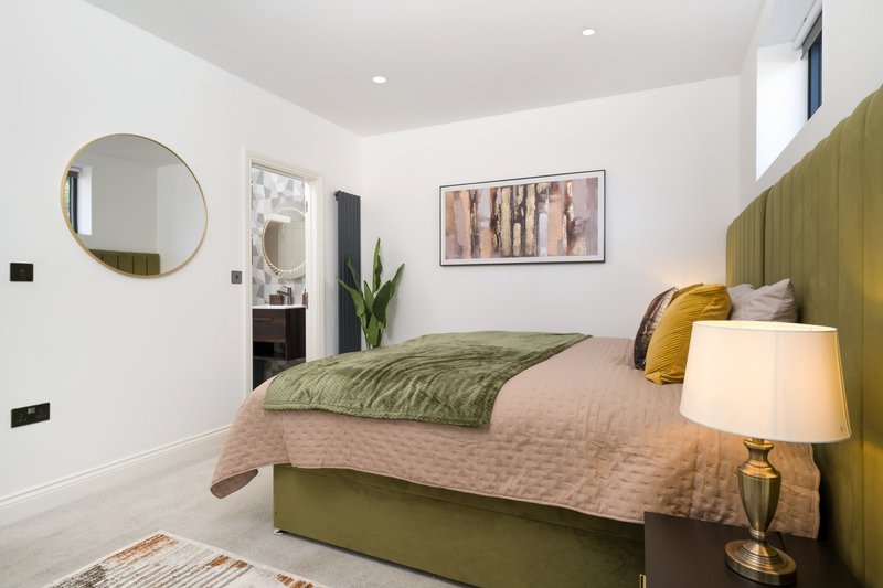 Modern bedroom with olive-green upholstered bed, table lamp, round mirror and framed wall art