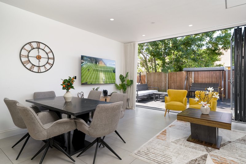 Open-plan living and dining area with modern furniture, wall clock, TV, and access to garden patio
