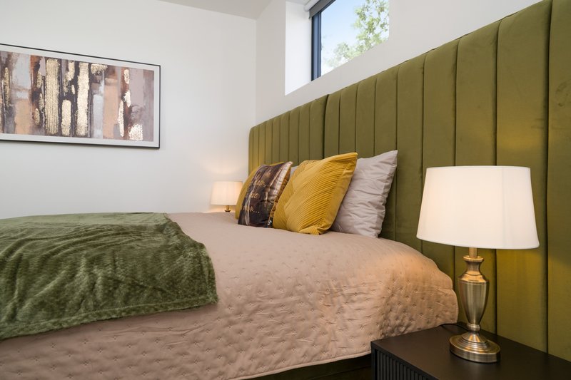 Modern bedroom with green upholstered headboard, double bed, bedside lamp and framed artwork