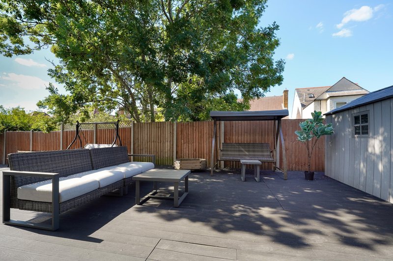 Outdoor patio with wooden fence, seating area, garden furniture and mature tree