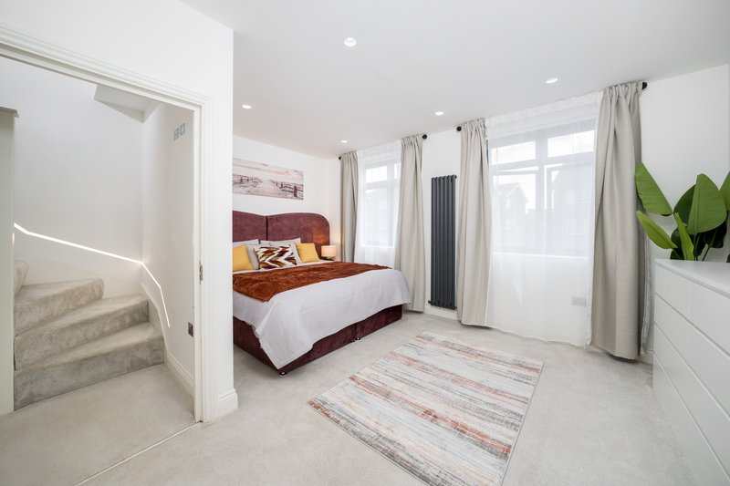 Bright modern bedroom with burgundy bed, white bedding, large windows and potted plant