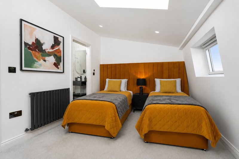 Bright twin bedroom with orange bedding, wooden headboards, framed artwork and skylight