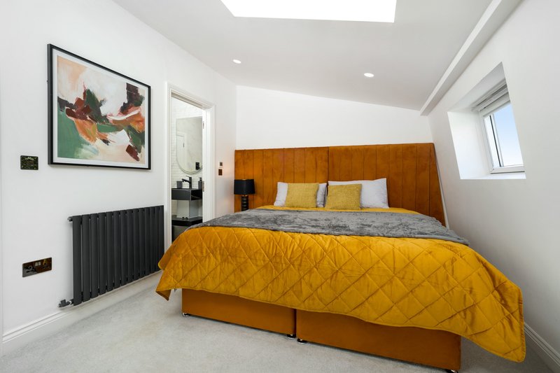 Bright bedroom with wooden headboard, yellow bedding, framed artwork and skylight