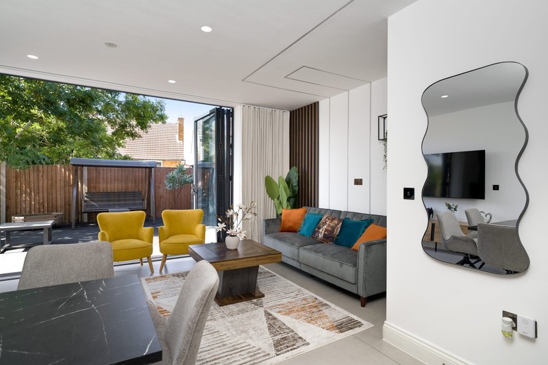 Modern open-plan living space with yellow armchairs, gray sofa, wavy mirror, and garden access