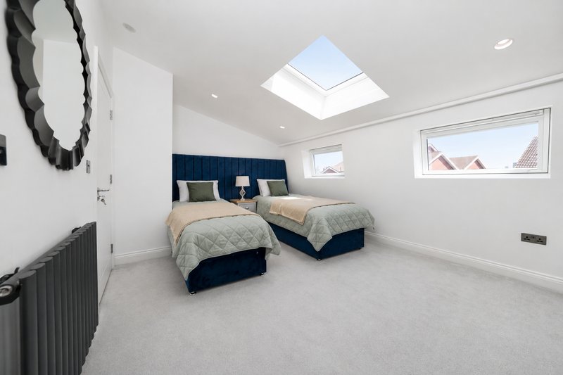 Bright attic bedroom with two single beds, skylight, radiator and framed artwork