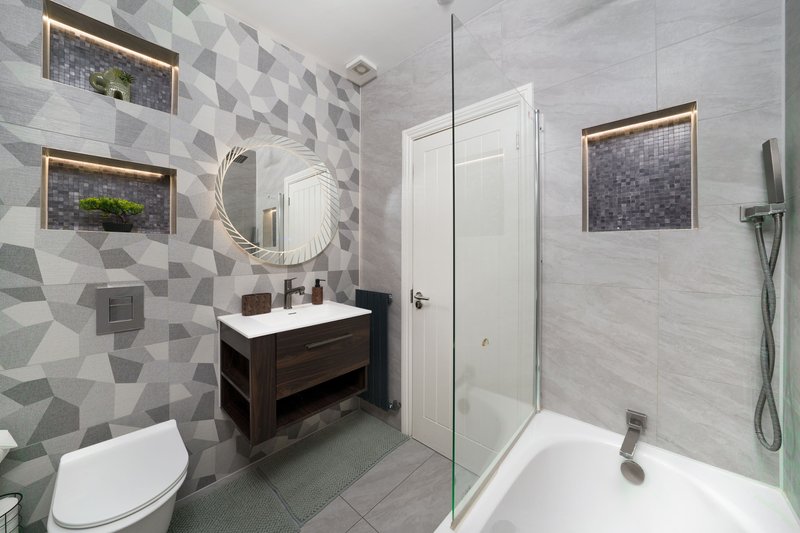 Modern bathroom with geometric tile walls, vanity sink, toilet, shower and circular mirror