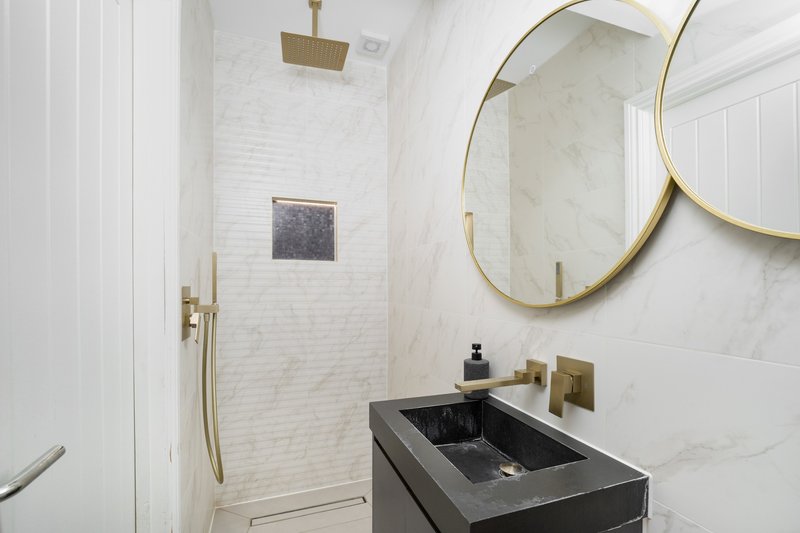 Modern bathroom with marble walls, black sink, gold mirror and brass fixtures