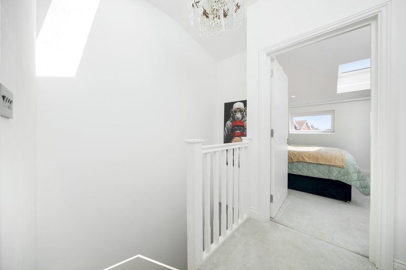 Bright hallway with white walls, skylight, staircase with white railings and bedroom doorway