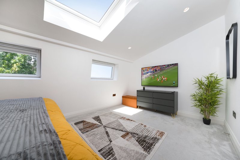 Modern bedroom with bed, TV mounted on wall, skylight and potted plant