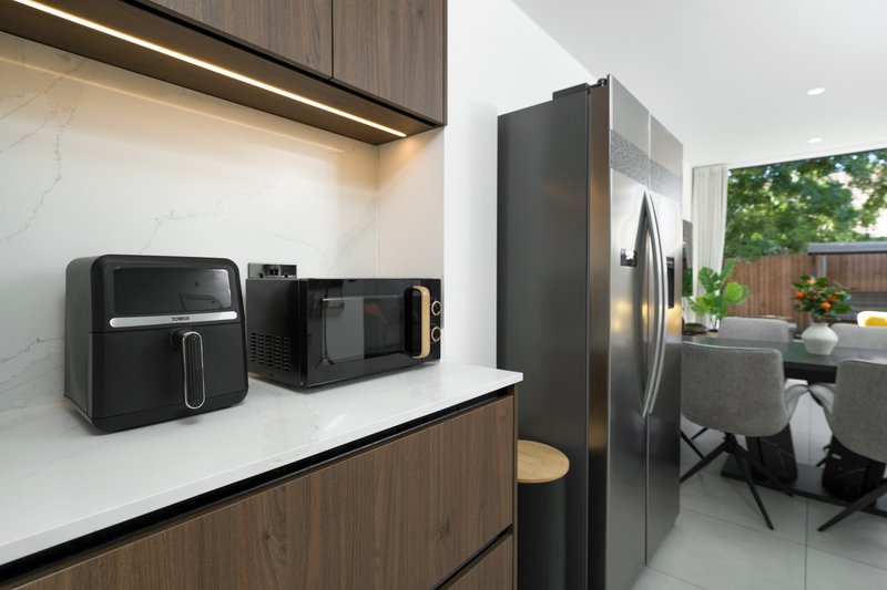 Modern kitchen with black appliances, marble countertop, wooden cabinetry and garden view