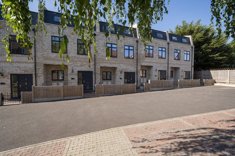 Modern brick townhouses with mansard roofs, wooden fencing, and paved driveway